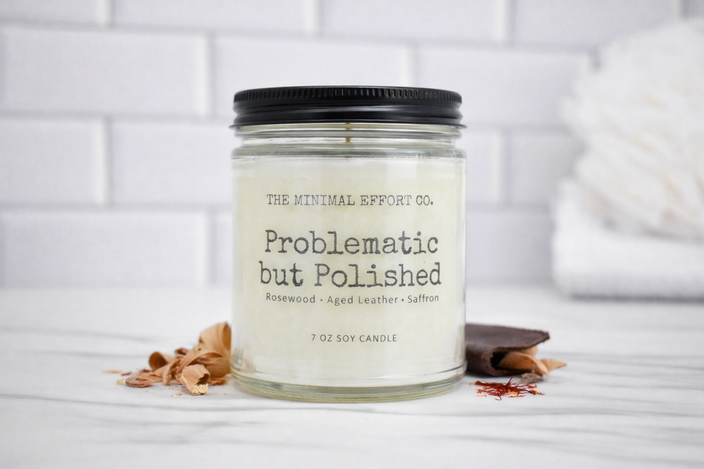 Candle jar labeled 'Problematic but Polished' by The Minimal Effort Co. on a white surface with a blurred background.