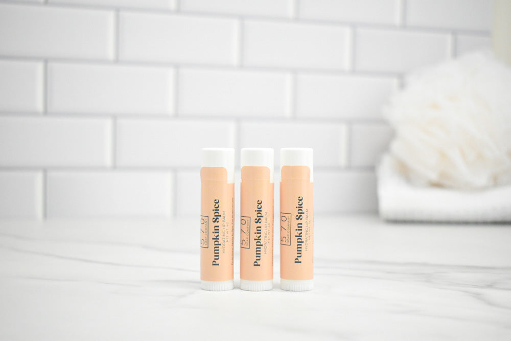 Three lip balm tubes labeled 'Pumpkin Spice' on a white surface with a tiled wall background.