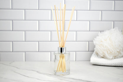 Clear diffuser bottle with wooden sticks on a white tiled wall background