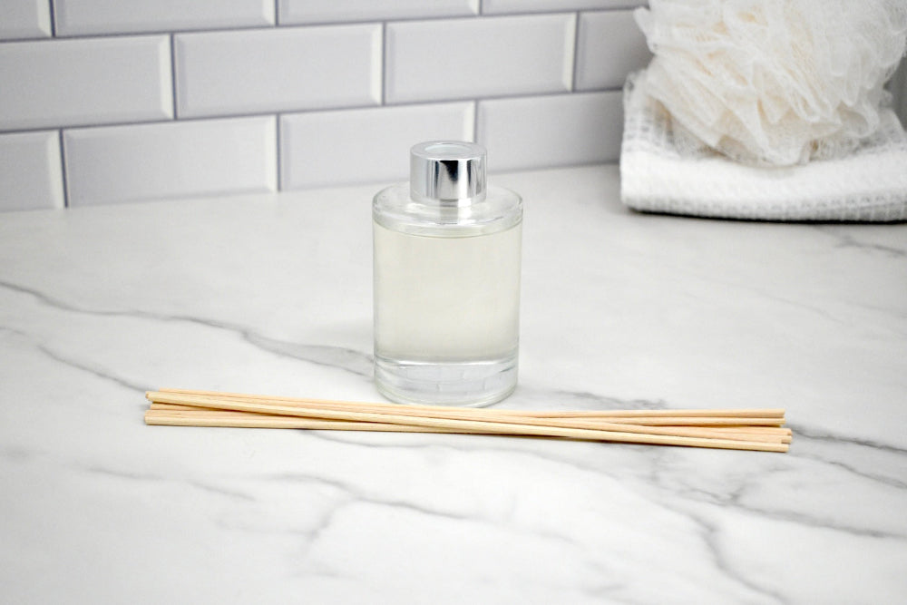 Clear diffuser bottle with wooden sticks on a marble surface with a tiled wall background
