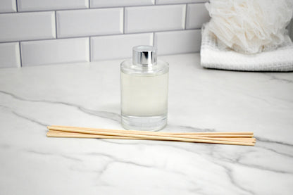 Clear diffuser bottle with wooden sticks on a marble surface with a tiled wall background