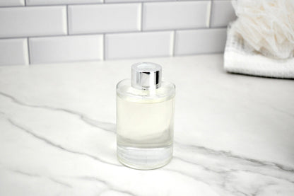 Clear glass candle with silver lid on a marble surface with white tiled wall background