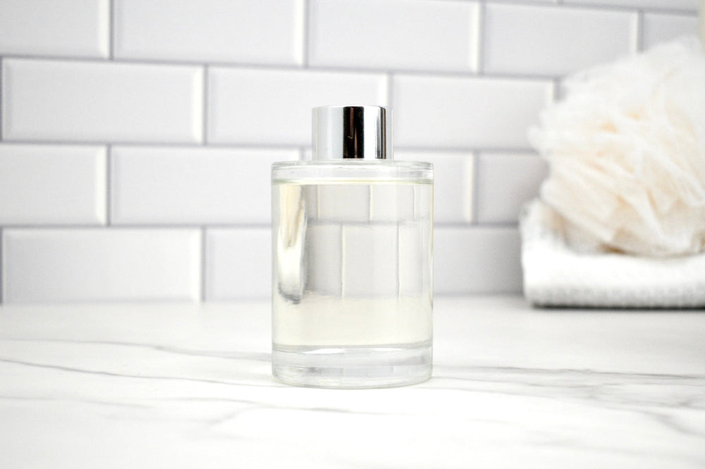 Clear glass bottle with silver cap on a white surface with a tiled wall background