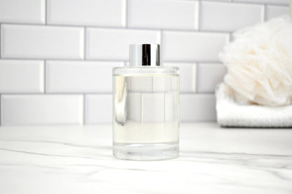 Clear glass bottle with silver cap on a white surface with a tiled wall background