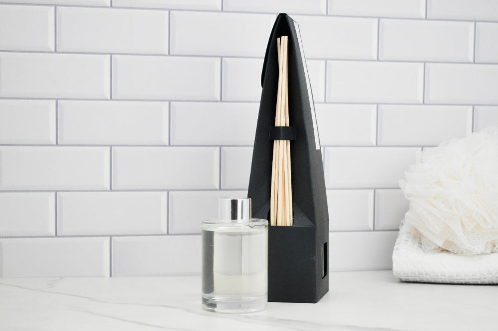 Black diffuser with wooden sticks on a white surface against a white tiled wall.