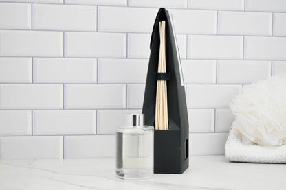 Black diffuser with wooden sticks on a white surface against a white tiled wall.