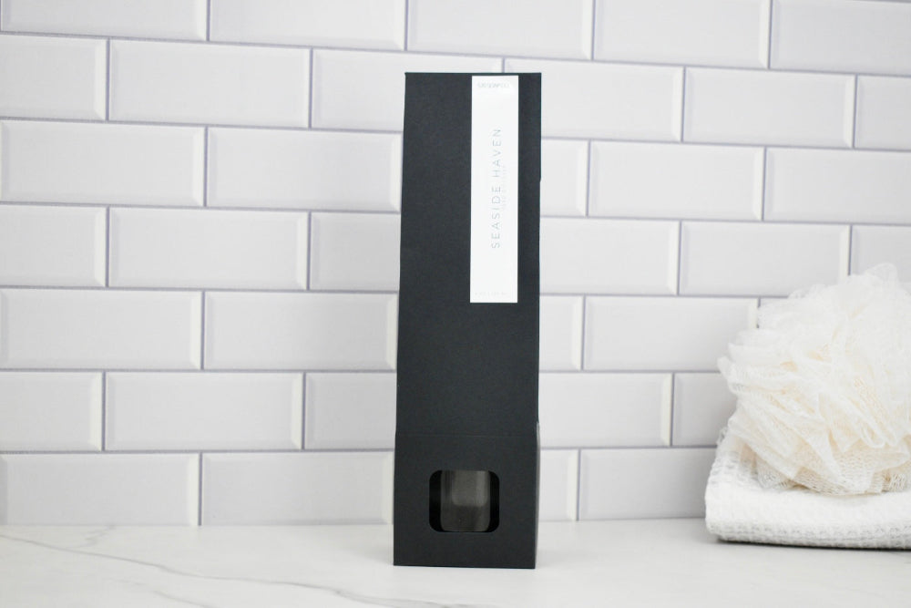 Black rectangular product packaging with a white label on a white tiled wall background