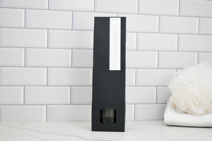 Black rectangular product packaging with a white label on a white tiled wall background