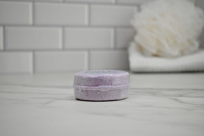 Purple bath bomb on a white surface with a blurred bathroom background