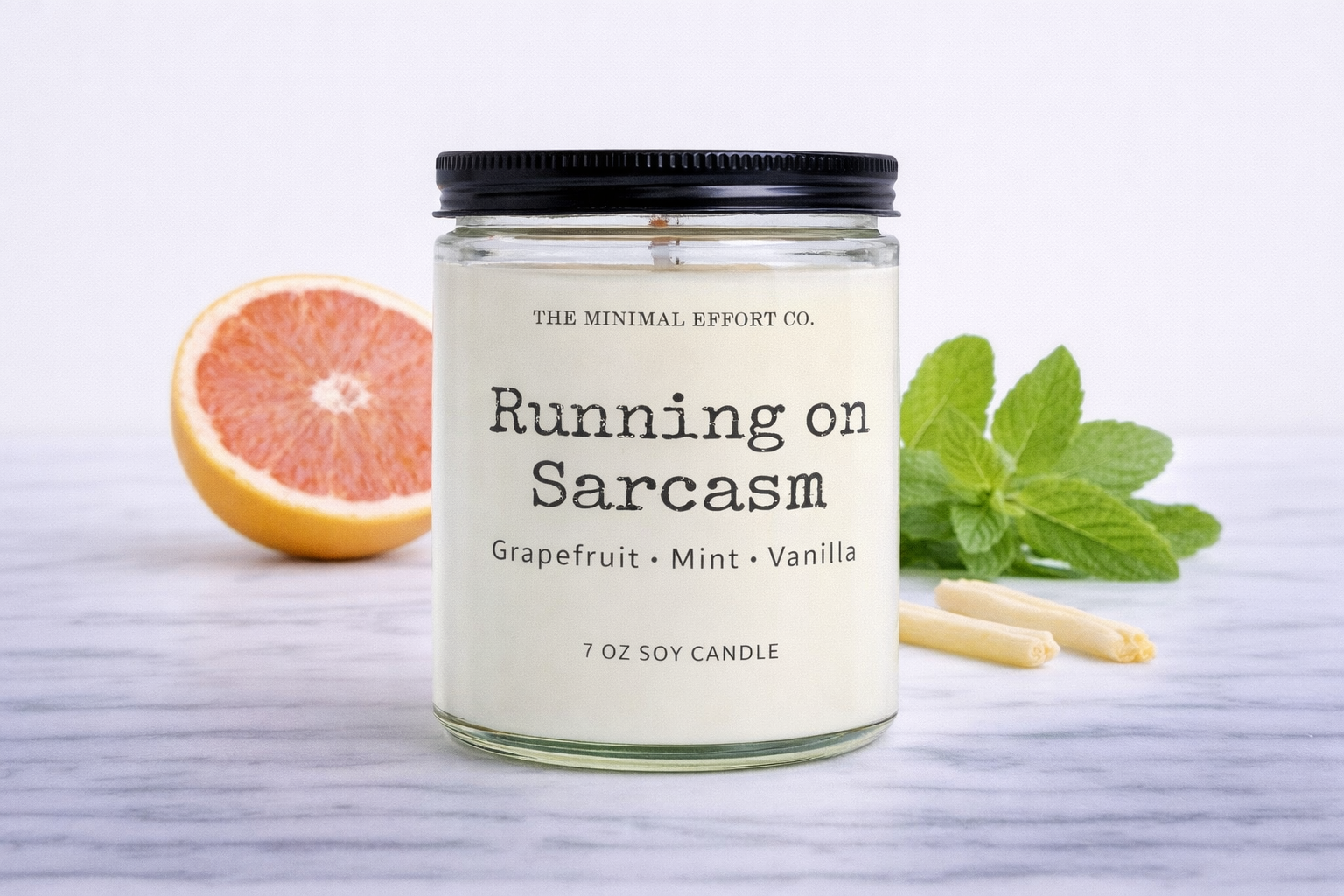 Candle labeled 'Running on Sarcasm' with grapefruit and mint leaves on a light background
