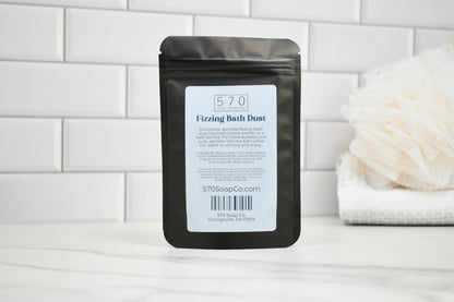 Packaging of 570 Fizzing Bath Dust on a bathroom counter with a white towel and bath bomb in the background.