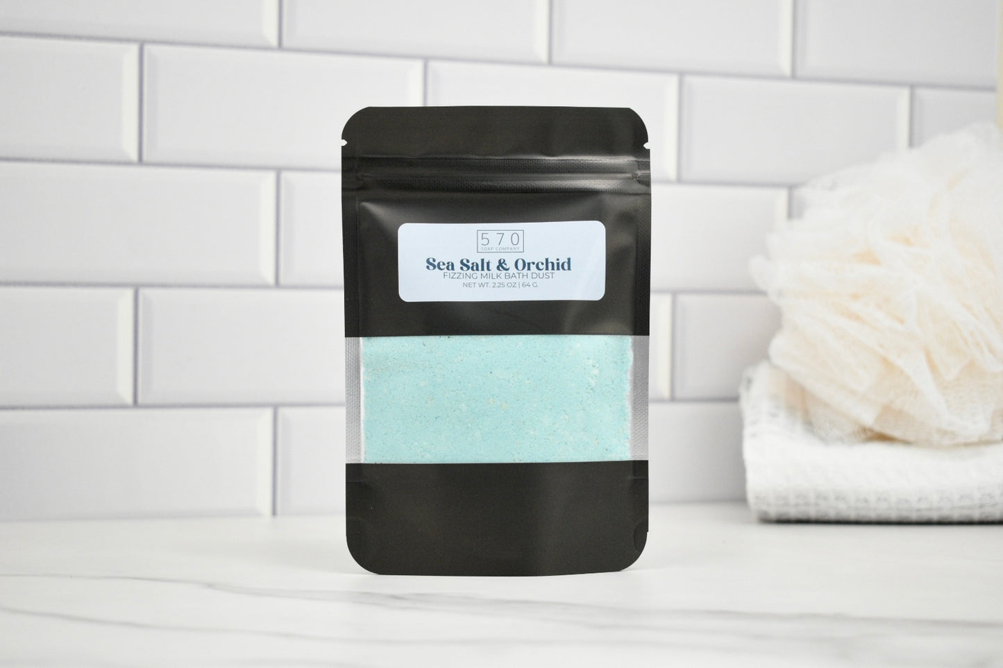 Black packaging of sea salt and orchid on a white tiled background