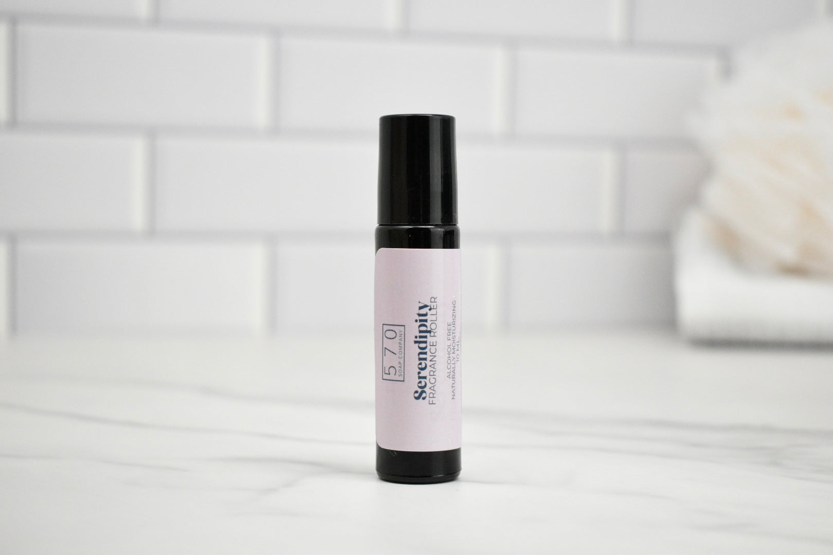 Skincare serum bottle with pink label on a white surface with a tiled wall background