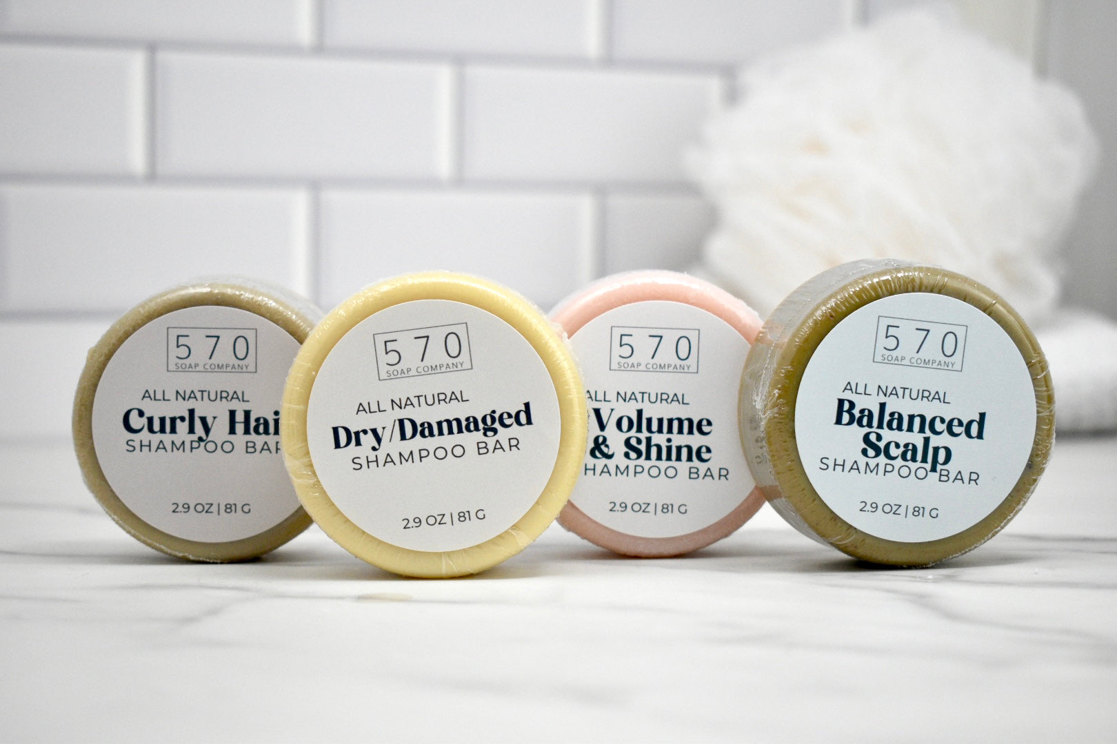 Four shampoo bars with labels on a white surface against a tiled wall background