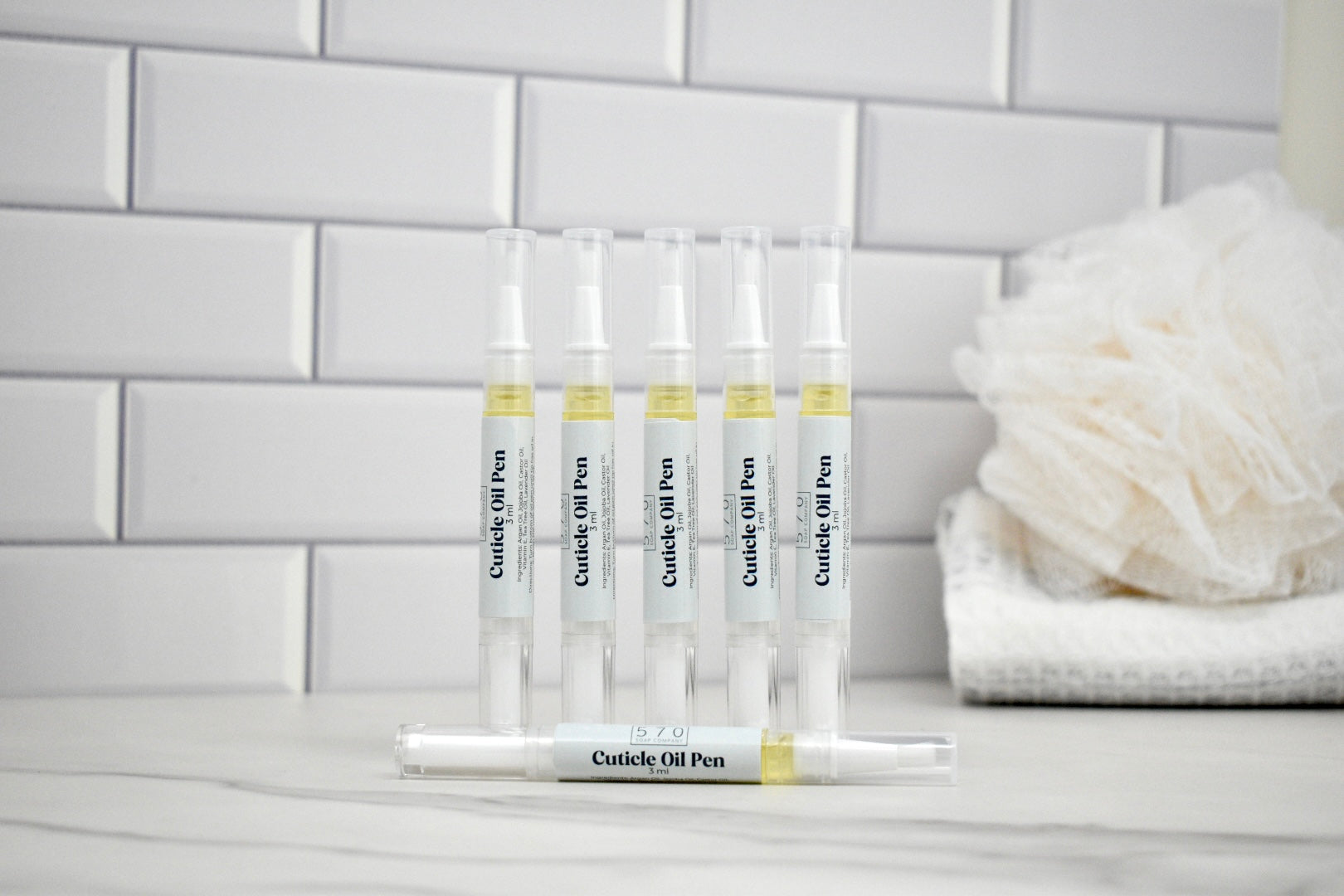 Set of cuticle oil pens on a stand with a white tiled wall background