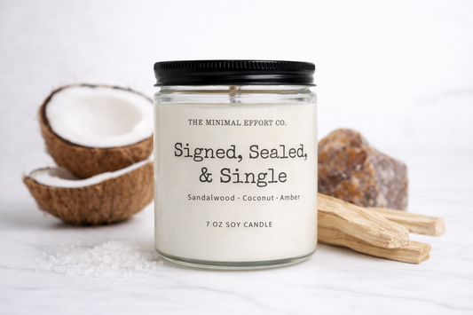 Candle labeled 'Signed, Sealed, & Single' with coconuts and a stick on a light background