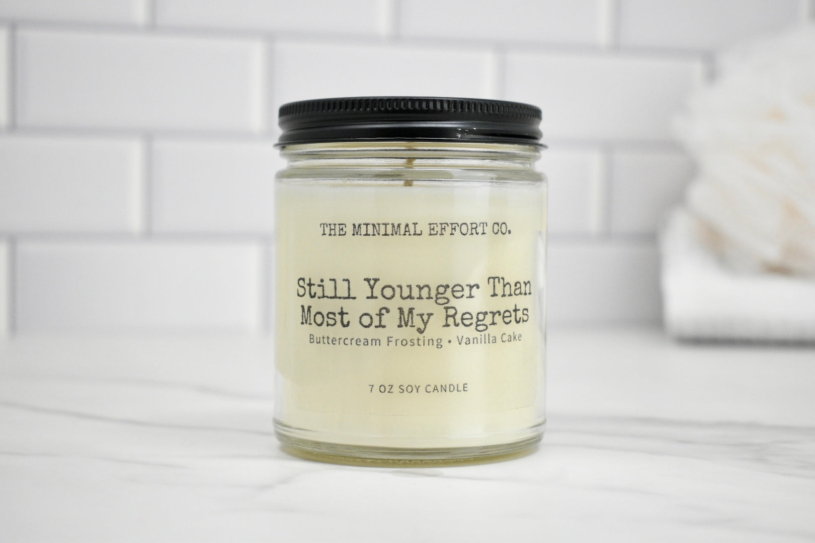 Candle in a glass jar with a black lid on a white surface