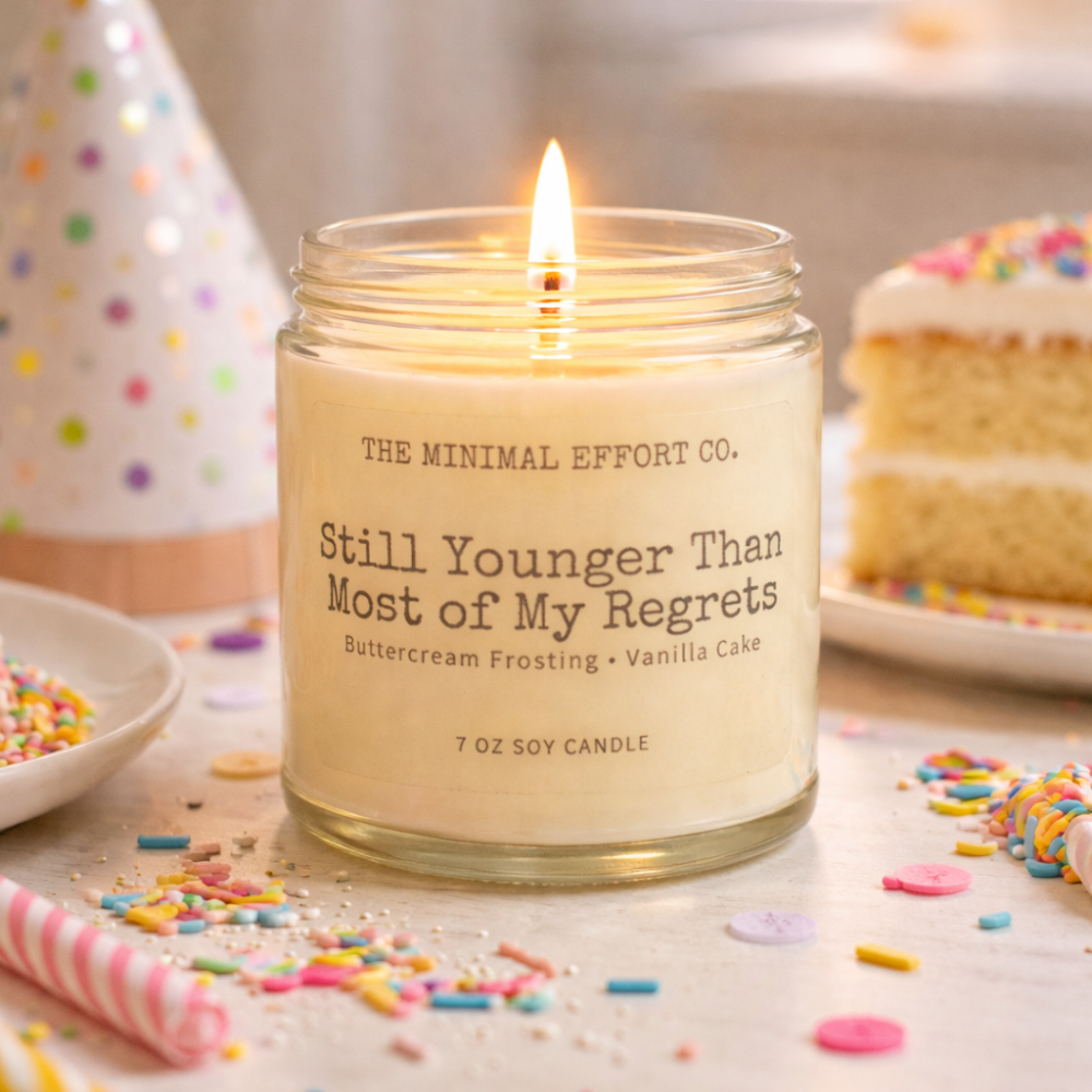 Candle in a glass jar with text, surrounded by birthday-themed items on a table.