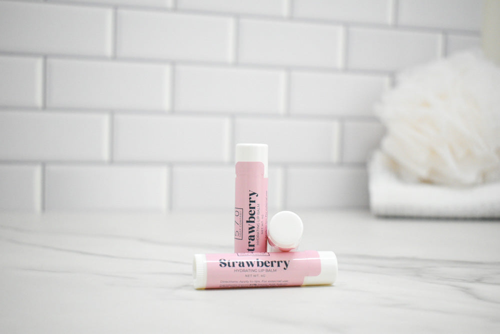 Two lip balm tubes labeled 'Strawberry' on a white surface with a tiled wall background.