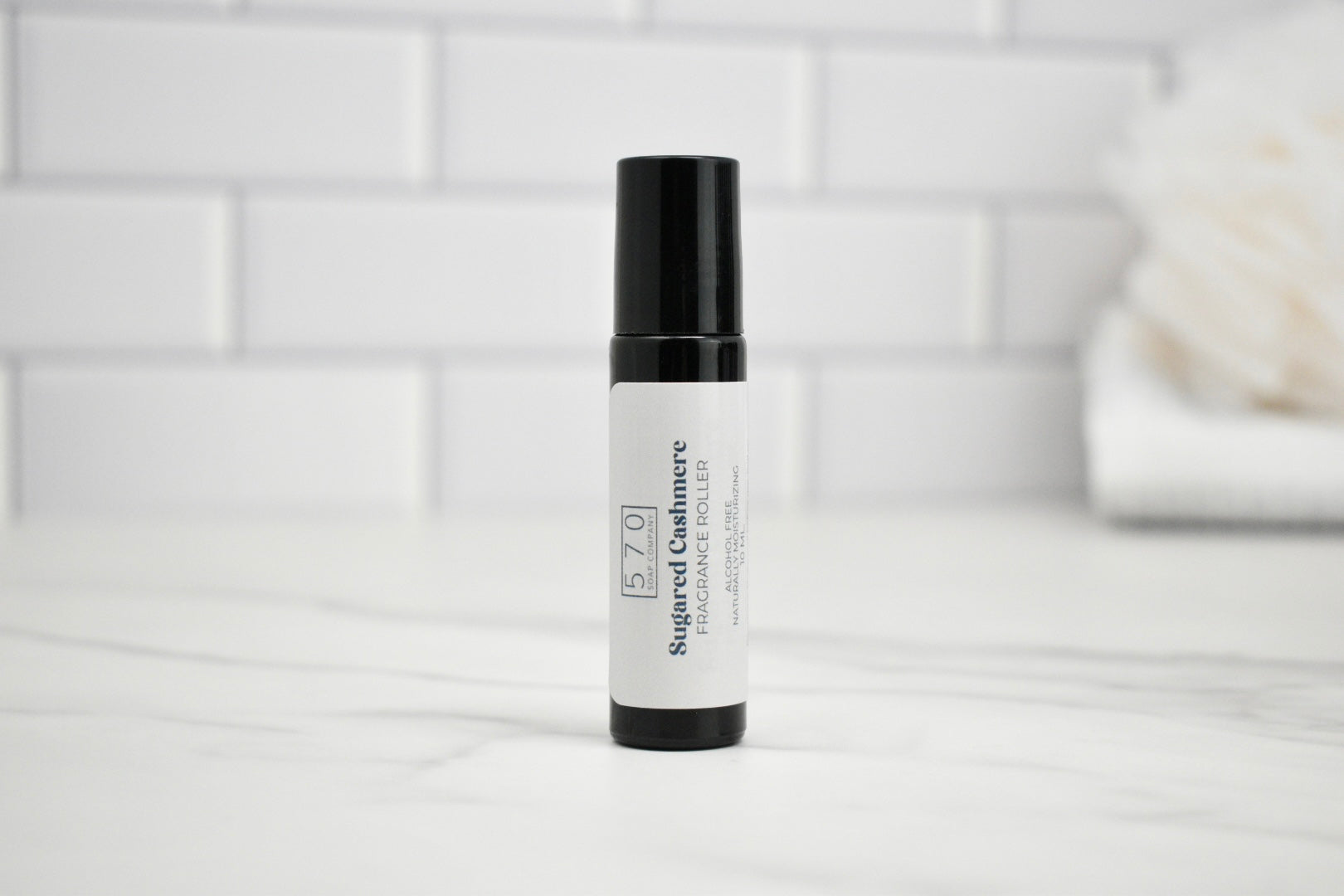 Skincare serum bottle with black cap on a white surface against a light tiled wall background