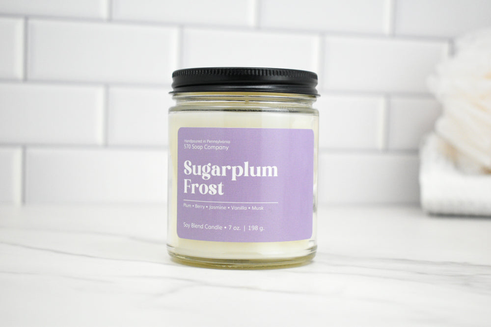 Candle jar labeled 'Sugarplum Frost' on a white surface with a tiled wall background