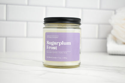 Candle jar labeled 'Sugarplum Frost' on a white surface with a tiled wall background