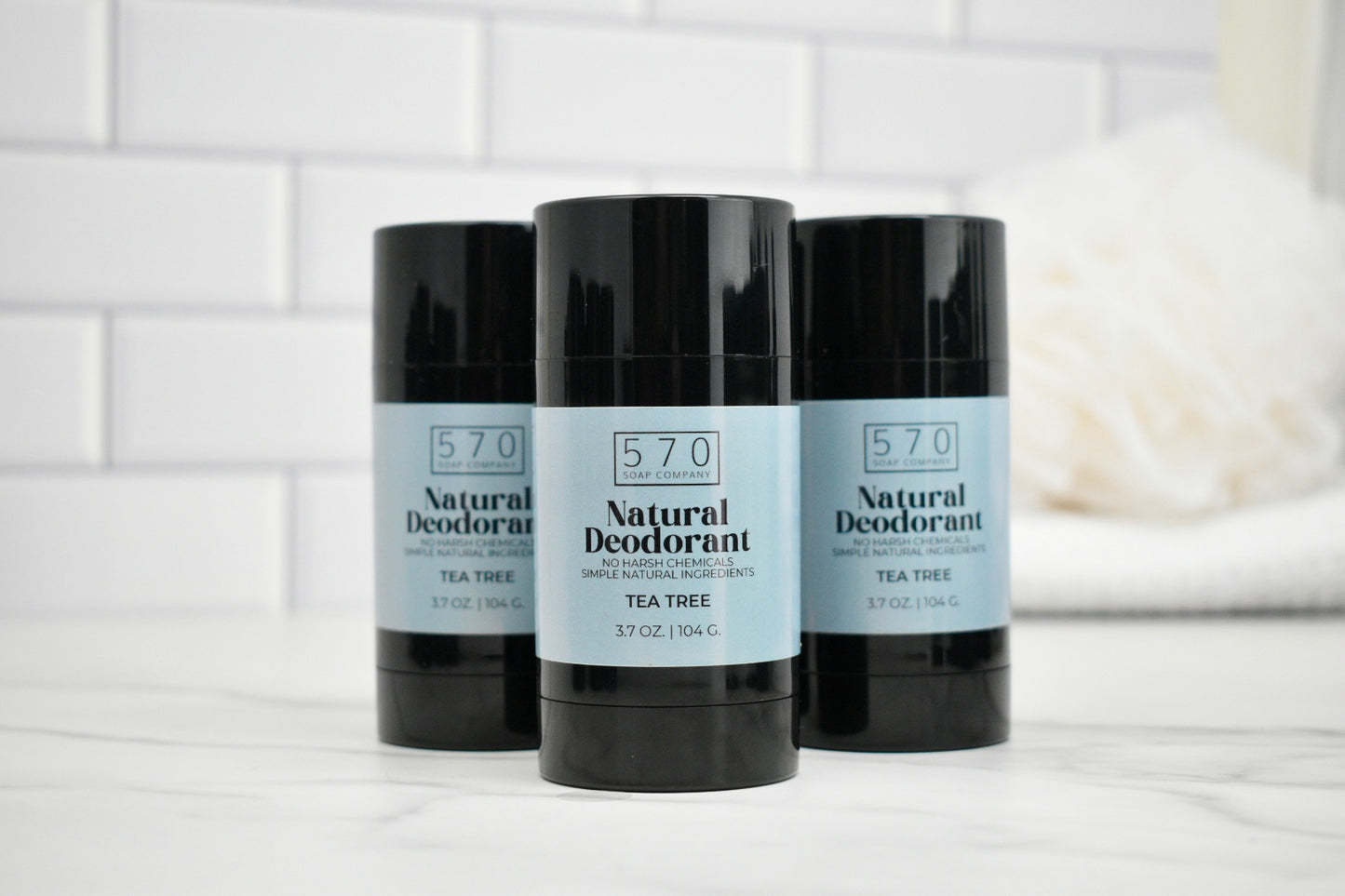 Three bottles of 570 Natural Deodorant on a white surface with a tiled wall background.