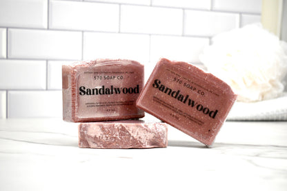 Three bars of Sandalwood soap from 570 Soap Co on a white surface with a tiled wall background.