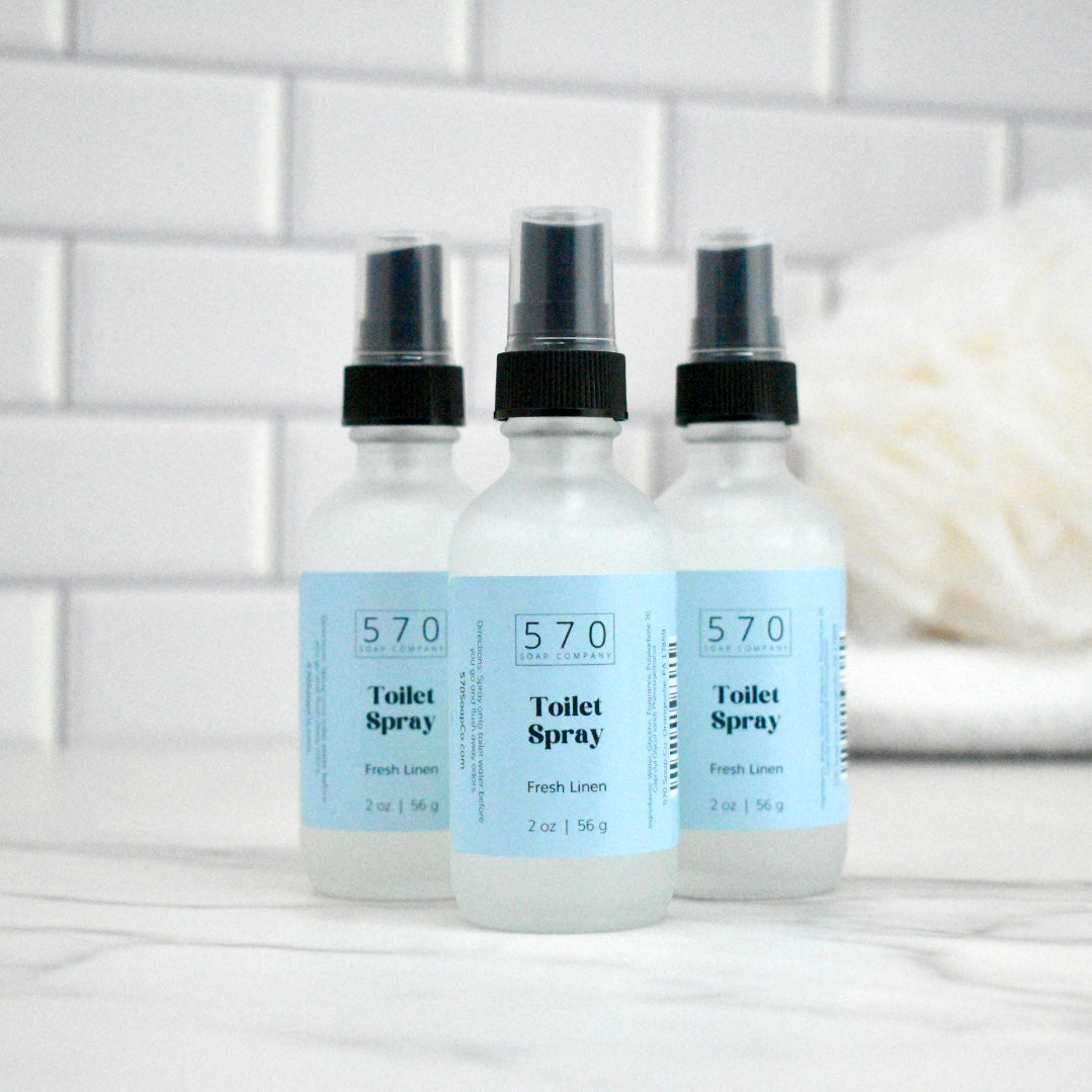 Three bottles of 570 Toilet Spray on a bathroom counter with a tiled wall background.