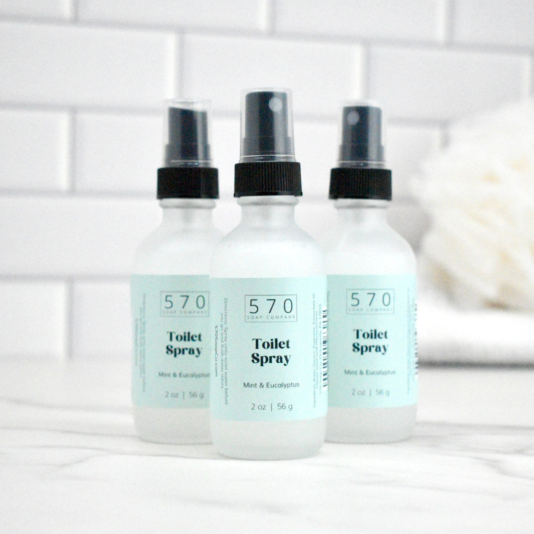 Three bottles of 570 Toilet Spray on a white surface with a tiled wall background.