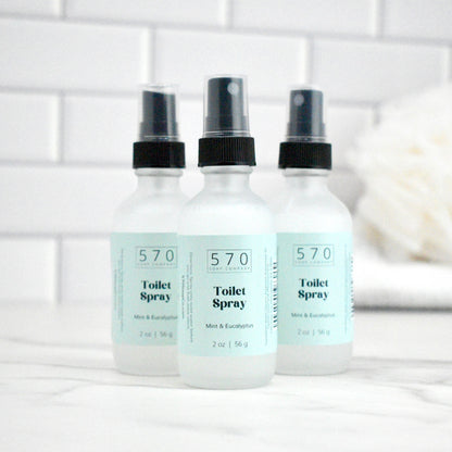 Three bottles of 570 Toilet Spray on a white surface with a tiled wall background.