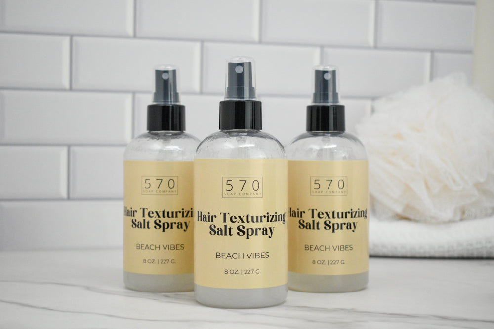 Three bottles of 570 Hair Texturizing Salt Spray on a white surface with a tiled wall background.