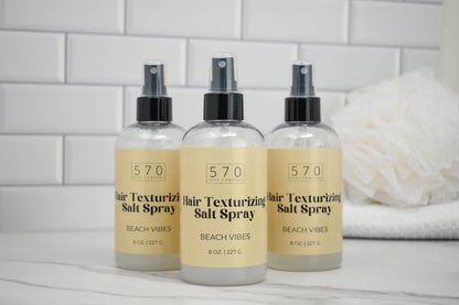 Three bottles of 570 Hair Texturizing Salt Spray on a white surface with a tiled wall background.