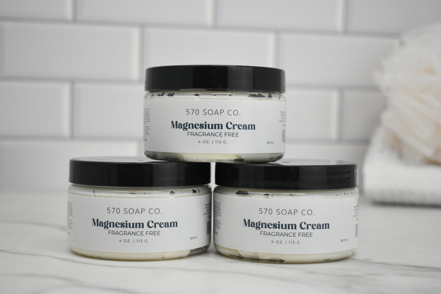 Three jars of 570 Soap Co. Magnesium Cream on a bathroom counter with a tiled wall background.