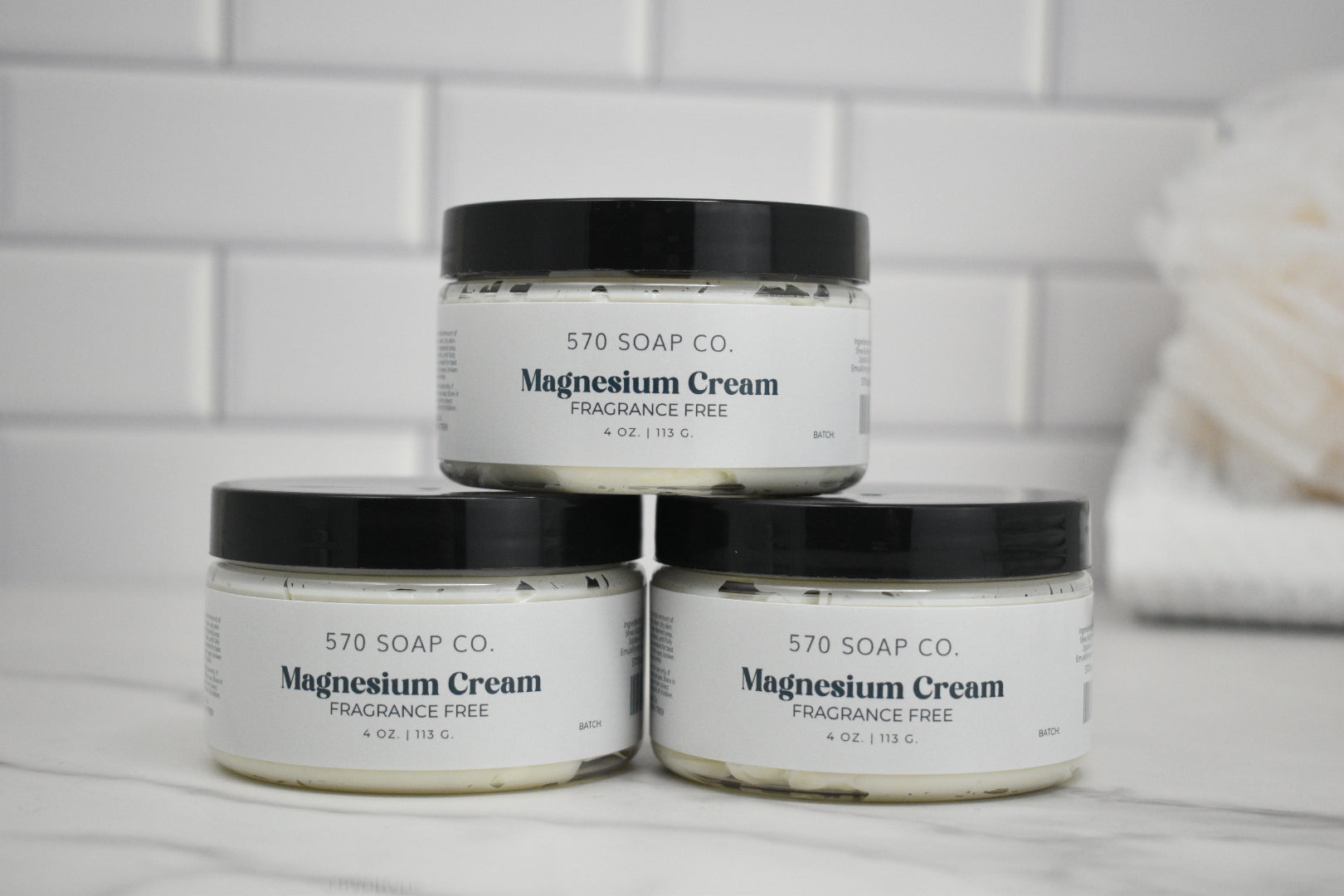 Three jars of 570 Soap Co. Magnesium Cream on a bathroom counter with a tiled wall background.