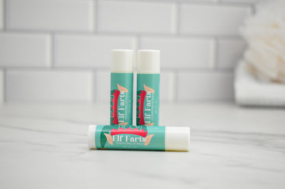 Three lip balm sticks with 'Elf Farts' branding on a bathroom counter.