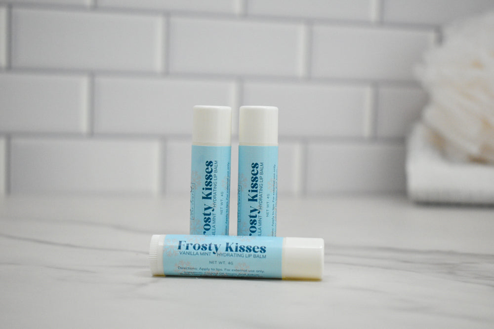 Three lip balm tubes labeled 'Frosty Kisses' on a bathroom counter with a tiled wall background.