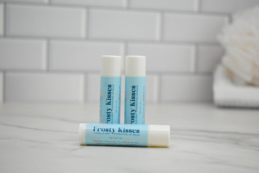 Three lip balm tubes labeled 'Frosty Kisses' on a bathroom counter with a tiled wall background.