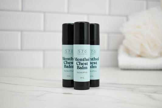 Three sticks of 570 Menthol Chest Balm on a white surface with a tiled wall background.