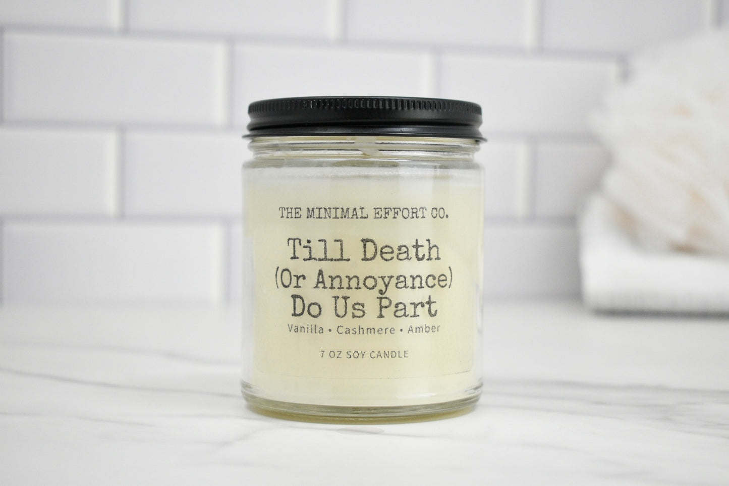 Candle jar labeled 'Till Death (Or Annoyance) Do Us Part' on a white surface with a tiled wall background.
