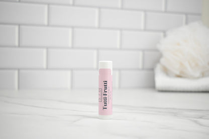 Pink lip balm tube on a white surface with a tiled wall background