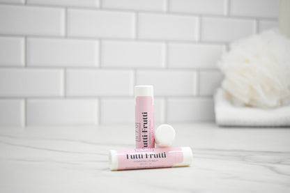 Two lip balm tubes with 'Tutti Frutti' branding on a bathroom counter.