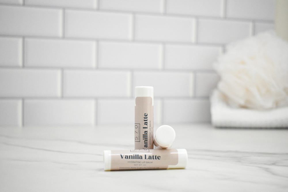 Two lip balm tubes labeled 'Vanilla Latte' on a white surface with a tiled wall background.