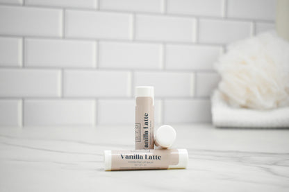 Two lip balm tubes labeled 'Vanilla Latte' on a white surface with a tiled wall background.