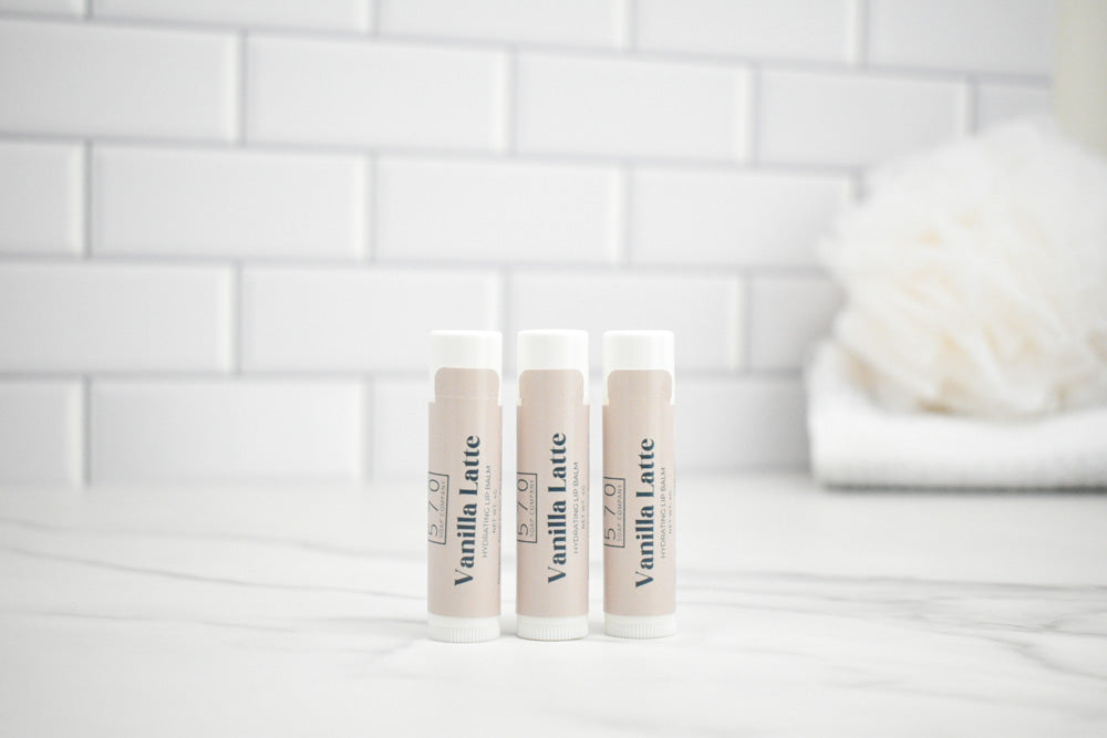 Three lip balm tubes labeled 'Vanilla Latte' on a white surface with a tiled wall background.