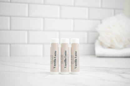 Three lip balm tubes labeled 'Vanilla Latte' on a white surface with a tiled wall background.