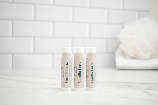 Three lip balm tubes labeled 'Vanilla Latte' on a white surface with a tiled wall background.