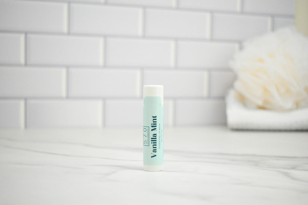 Lip balm tube labeled 'Vanilla Mint' on a white surface with a tiled wall background