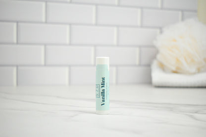 Lip balm tube labeled 'Vanilla Mint' on a white surface with a tiled wall background