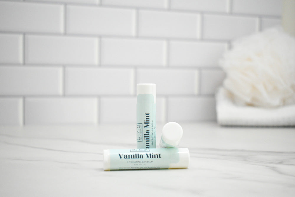 Two lip balms labeled 'Vanilla Mint' on a bathroom counter with a tiled wall background.